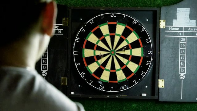 Man throwing a dart arrow in target center of dartboard in game of darts. 4K