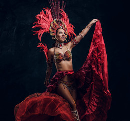Talented joyful can can dancer in red feather costume is posing at small dark studio.