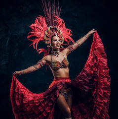 Talented joyful can can dancer in red feather costume is posing at small dark studio.