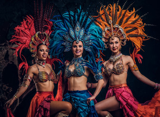 Three beautiful young womans in traditional brasilian carnaval costumes are posing for photographer at studio.