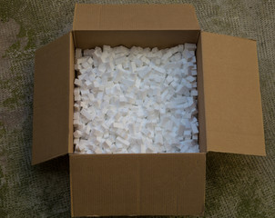 cardboard box with packing foam pellets white polystyrene foam, styrofoam popcorn or packing noodles used to cushion the contents of packages while shipping commonly made of expanded polystyrene foam