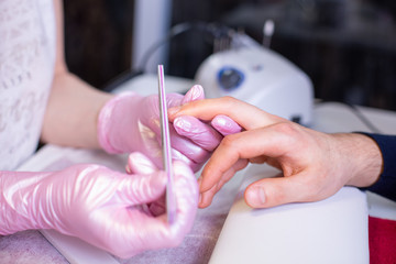 Professional manicure of male hands in a beauty salon close up. Master in gloves makes a manicure...
