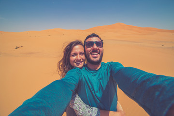 Happy tourist smiling take photo selfie in the Middle of the red Sahara desert with giant red dunes in background. Merzouga, Morocco, Africa