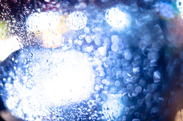 Rain drops on car window with road light bokeh, City life in night in rainy season abstract background,water drop on the glass, night storm raining car driving concept.