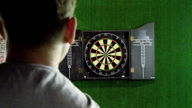 Man throwing a dart arrow in target center of dartboard in game of darts. 4K