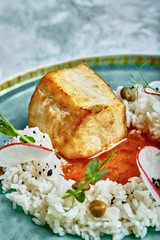 Cod steak with rice and sauce on a blue plate on a background of concrete.