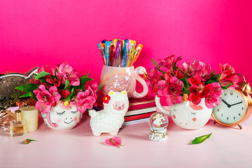 Different Notebooks, alarm clock, unicorn mug, llama squishy, Alstroemeria flowers and flamingo mug with colorful gel pens on bright pink background. Idea of Girly Desk table. Back to school concept