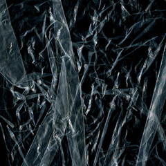 Transparent plastic wrap on the black background. Plastic bag texture. Reusable trash and waste.