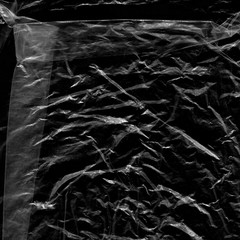 Transparent plastic wrap on the black background. Plastic bag texture. Reusable trash and waste.