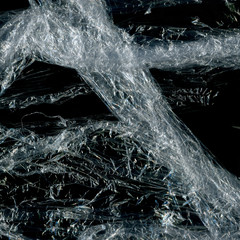 Transparent plastic wrap on the black background. Plastic bag texture. Reusable trash and waste.