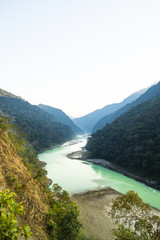 Stunning view of some green mountain peaks with the Sacred Ganges River flowing between them in Rishikesh, India.