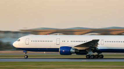 Wide-body passenger airplane taxing on runway for take off at sunset, side view, in motion....