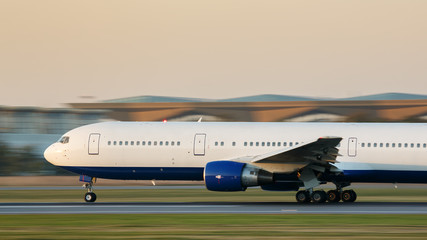 Wide-body passenger airplane taxing on runway for take off at sunset, side view, in motion. Vacation, aviation, travel, trip concept. Departure board. Copy space. 