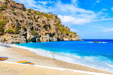 Obraz premium Young woman tourist standing on idyllic Achata beach and looking at azure sea, Karpathos island, Greece