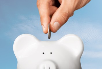 Hand putting coin to piggy bank and coins on white background
