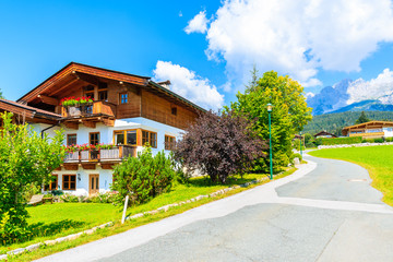 Road and traditional alpine houses in village of Going am Wilden Kaiser on beautiful sunny summer day with Alps mountains in background, Tirol, Austria