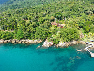 Aerial view of tropicsal house in forest surrounded by trees and next to the ocean and blue turquoise water. luxurious villa and spacious pavilion next to the sea, Brazil.