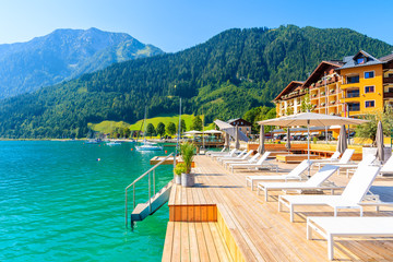 Pier with chairs on sunny terrace on shore of beautiful Achensee lake on sunny summer day with blue sky, Karwendel mountain range, Tirol, Austria - obrazy, fototapety, plakaty