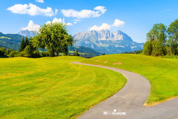 Way for electric cars on green golf course area against mountains background on sunny summer day, Kitzbuhel, Tyrol, Austria