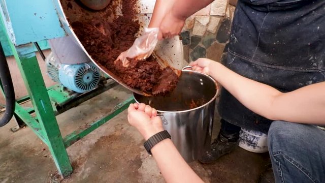 Side view. Woman making Mole in Puebla Mexico. North America. Two people taking out some ingredients from the grinder. Cooking Traditional recipe.