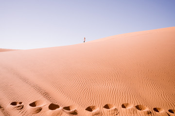 Windswept sand dunes with distant lone figure and camel footprints , in the Sahara Desert, Morocco, Africa