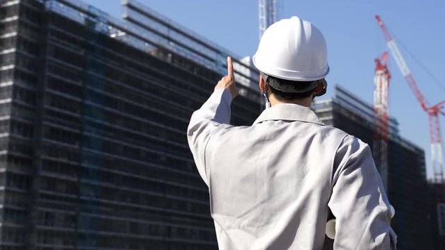 図面を抱え建設現場を見つめるビジネスマン　指差し