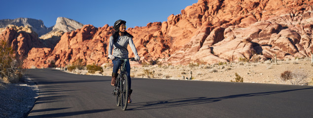 fit african american woman riding bicycle on road in red rock canyon park panorama