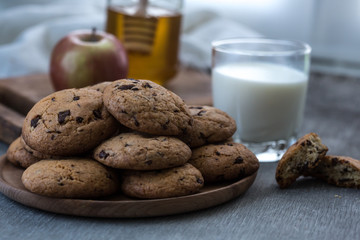 Pile of Delicious Chocolate Chip Cookies on a plate with glass of milk on wooden table