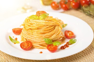 Spaghetti pasta with cherry tomatoes and basil leaves on white plate