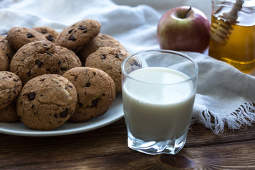 Pile of Delicious Chocolate Chip Cookies on a plate with glass of milk on wooden table