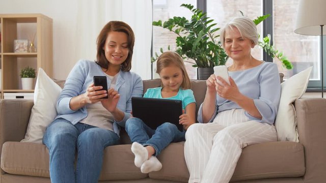 family, technology and three generations concept - happy mother, daughter and grandmother with tablet computer and smartphones at home