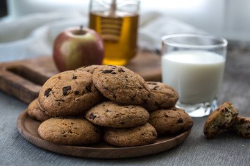 Pile of Delicious Chocolate Chip Cookies on a plate with glass of milk on wooden table