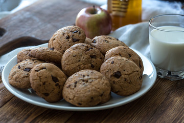 Pile of Delicious Chocolate Chip Cookies on a plate with glass of milk on wooden table
