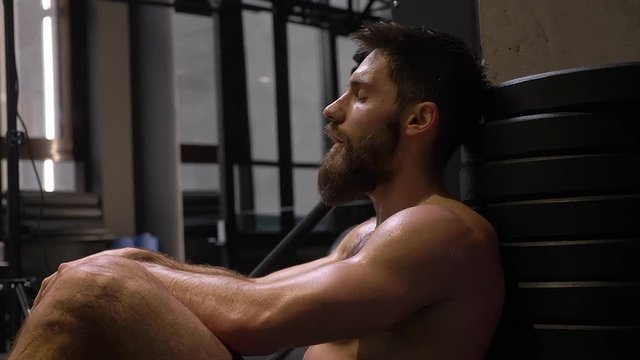 Closeup shoot of adult muscular athletic man sitting and being tired indoors in the gym