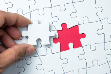 Hand putting the last piece of white jigsaw puzzle on red background and place for your content