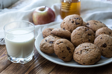 Pile of Delicious Chocolate Chip Cookies on a plate with glass of milk on wooden table