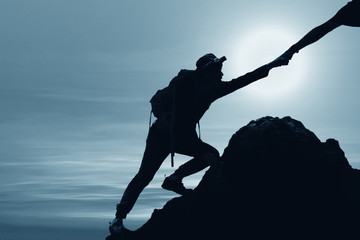 silhouette of man climbing up mountain with hand giving help