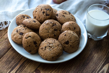 Pile of Delicious Chocolate Chip Cookies on a plate with glass of milk on wooden table