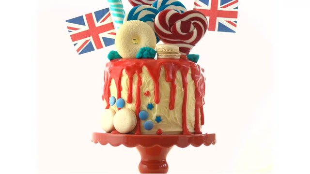 UK on-trend candyland fantasy drip cake with red, white and blue decorations, lollipops and flags on white background.