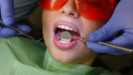 Girl patient in dental clinic. Dentist makes routine inspection of teeth and gums. Close-up.
