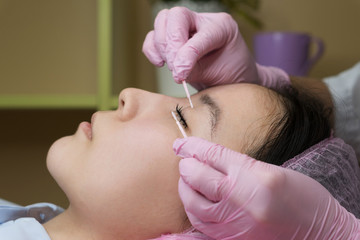 Eyelash extension procedure. Female eyes with long eyelashes. Cosmetic procedure in spa salon. Beautician corrects the shape of false eyelashes