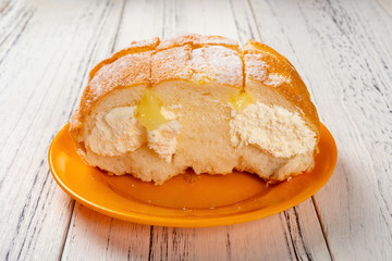 side view bread with cream inside with half eaten on wood table