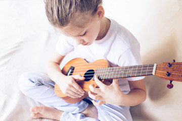 A little girl plays guitar in her home. Selective focus. Close-up. The concept of music and art.