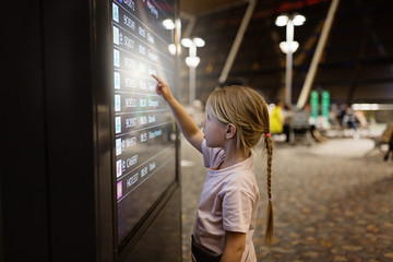 Cute little girl pressing icon on digital touch screen in airport terminal. Kid using technology 