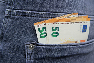 a few banknotes of 50 euros in the back pocket of men's gray-blue jeans, close-up