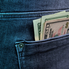 banknotes of 20 and 50 American dollars are in the back pocket of men's gray-blue jeans, square,...
