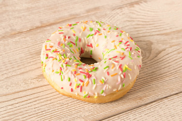 Fresh glazed donut with colorful sprinkles on a wooden table.