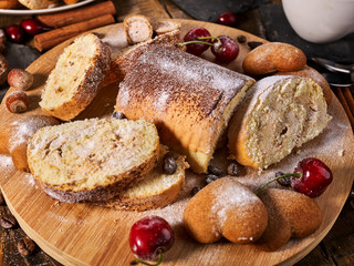 Rolled biscuit and sand chocolate cookies on board. Cinnamon stick and cherry on kitchen wood table in rustic style. Cherry in powdered sugar.