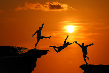Fototapeta na wymiar The concept of betrayal and the help of friends, Silhouette of Men are jumped between high cliff at a red sky sunset