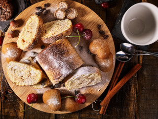Rolled biscuit and sand chocolate cookies on board. Cinnamon stick and cherry on kitchen wood table in rustic style. Supplement for breakfast. Top view.